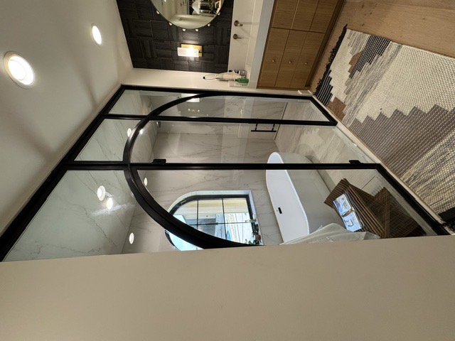 Black steel-framed arched glass shower enclosure beside a freestanding tub by West Little Rock Glass