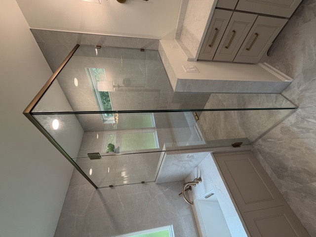 Frameless corner shower with brass header trim and marble tile by West Little Rock Glass, serving Conway