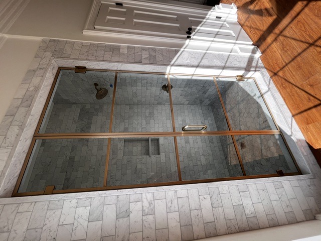 Brass gridded steel-look shower doors over carrara subway tile by West Little Rock Glass