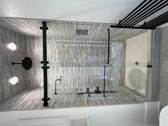 Sliding frameless shower door with matte black roller bar over stacked-stone tile by West Little Rock Glass, serving Cabot