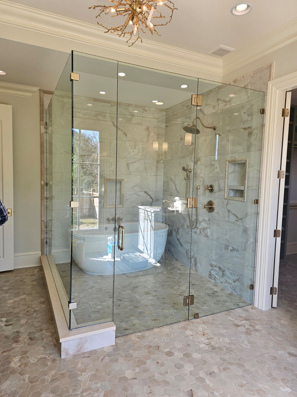 Full-height frameless glass enclosure wrapping a soaker tub with brass hardware by West Little Rock Glass
